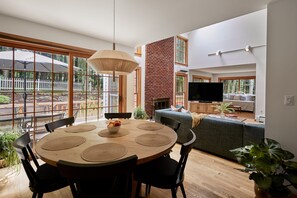 A modern living room with a fireplace, a dining area with a round table and chairs, and a large window overlooking a garden. - Perfect Nature Haven In Great Barrington (Great Barrington)