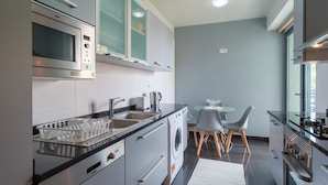 Une cuisine moderne dotée d’appareils électroménagers en acier inoxydable, d’un lave-linge encastré et d’un coin repas avec une table et des chaises en verre.
