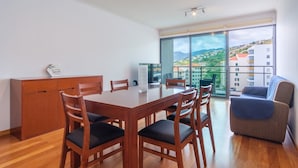 Un salon moderne avec une table et des chaises en bois, un canapé et une grande fenêtre donnant sur des immeubles et des collines.