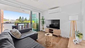 A modern living room with a sofa, TV, and a balcony with a view of greenery and buildings.