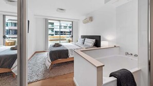 A modern bedroom with a large bed, a separate bathroom, and a view of the outside.