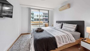 A bedroom with a bed, a TV, a window, and a bedside table.