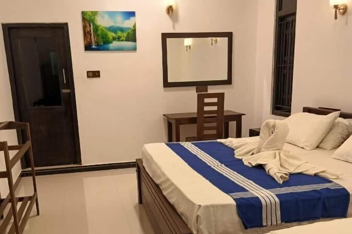 Habitación de hotel con dos camas, un escritorio, una silla, una puerta, un espejo y un cuadro en la pared.