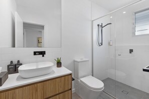 Een moderne badkamer met een groot wit wastafelmeubel, toilet en een douchecabine met glazen wanden.