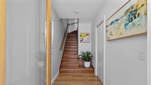 Un pasillo con una escalera de madera, una planta en maceta y dos cuadros en las paredes.