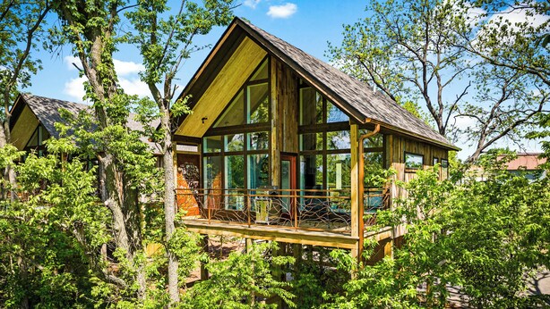 A wooden cabin with a glass balcony, surrounded by dense greenery. - Fairway Treehouses (Berryville)