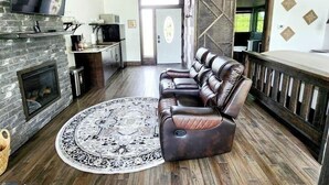 A spacious living area with a stone fireplace, leather sofa, and a large rug. - Fairway Treehouses (Berryville)