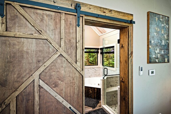 A rustic wooden door leading to a bathroom with a bathtub and a glass shower enclosure.