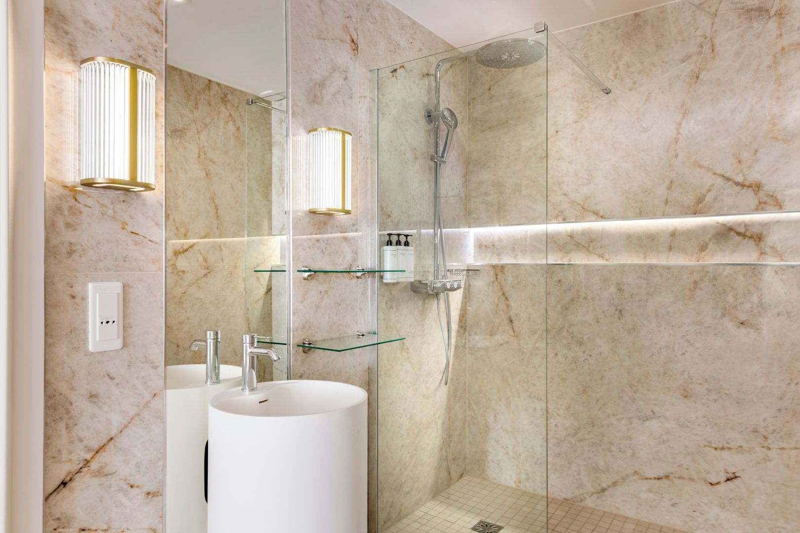 A modern bathroom with a glass-enclosed shower, marble walls, and a white sink with two faucets.