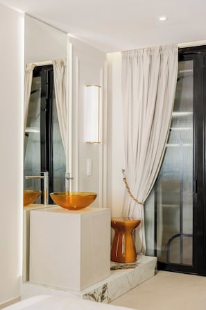 A modern bathroom with a large mirror, two gold-colored vessel sinks, a white pedestal, and a black door with a glass panel. - Merveil - Signature Suite -Tour Eiffel- Grenelle I (Paris)