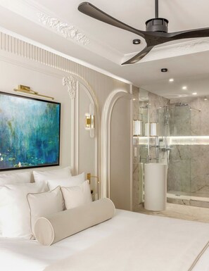 Un dormitorio moderno con una cama grande, un ventilador de techo, un cuadro y una zona de ducha de mármol.
