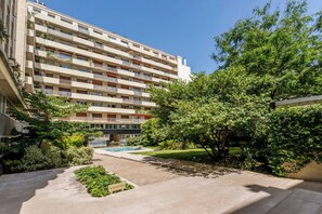 Un edificio residencial de varios pisos con balcones, un jardín con piscina y cielo despejado.