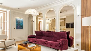 A living room with a plush red sofa, a glass coffee table, and a white armchair. There is a painting on the wall and a wooden floor. - Merveil - Signature Suite -Tour Eiffel- Grenelle I (Paris)