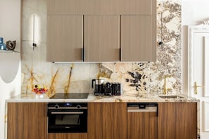 A modern kitchen with wooden cabinets, a marble backsplash, a built-in oven, a dishwasher, and a coffee maker. - Merveil - Signature Suite -Tour Eiffel- Grenelle I (Paris)