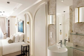 A modern bedroom with a large bed, a bedside table, and a nightstand. There is a large mirror with a marble backsplash and a built-in sink. - Merveil - Signature Suite -Tour Eiffel- Grenelle I (Paris)
