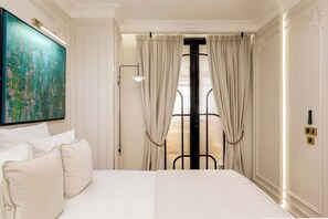 A hotel room with a large bed, a painting on the wall, a window with curtains, and a door with a remote control. - Merveil - Signature Suite -Tour Eiffel- Grenelle I (Paris)