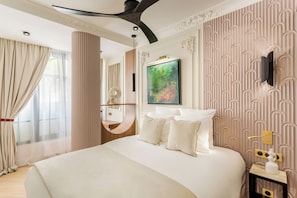 A modern hotel room with a large bed, a ceiling fan, a painting on the wall, and a decorative wall panel. - Merveil - Signature Suite -Tour Eiffel- Grenelle I (Paris)