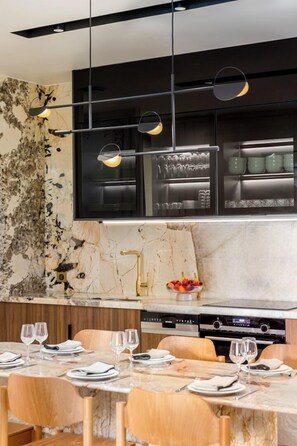 A modern kitchen with marble countertops, a built-in oven, and a dining area with wooden chairs and a marble table.