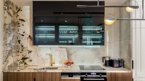 Una cocina moderna con salpicadero de mármol, armarios de madera, horno empotrado y un mueble superior de vidrio que exhibe utensilios de cocina.