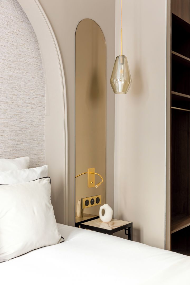 A hotel room with a bed, a large mirror, a small table with a tissue box, and a hanging light fixture.