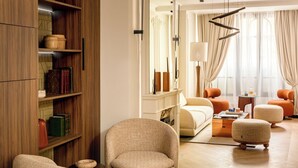 A well-lit living room with a fireplace, a bookshelf, and a seating area with a sofa and ottomans. - Merveil - Signature Suite -Tour Eiffel-Grenelle II (Paris)