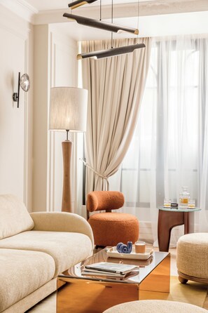 A modern living room with a sofa, armchair, and ottoman, a lamp, and a coffee table with books and a teapot. - Merveil - Signature Suite -Tour Eiffel-Grenelle II (Paris)