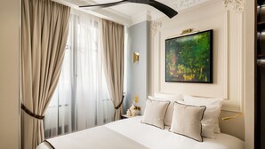A hotel room with a large bed, beige curtains, a painting on the wall, and a ceiling fan. - Merveil - Signature Suite -Tour Eiffel-Grenelle II (Paris)