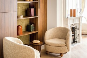A living room with a beige armchair, a wooden bookshelf, and a fireplace. - Merveil - Signature Suite -Tour Eiffel-Grenelle II (Paris)