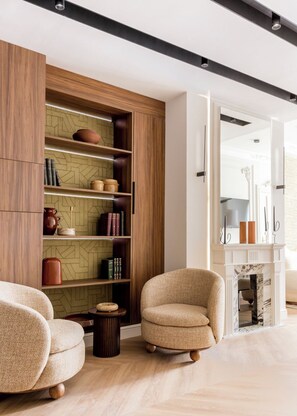 A modern living room with a wooden bookshelf, two armchairs, and a fireplace.