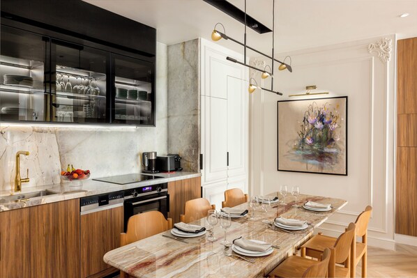 A modern kitchen with a marble countertop, stainless steel appliances, and a dining area with a marble table set for six. - Merveil - Signature Suite -Tour Eiffel-Grenelle II (Paris)