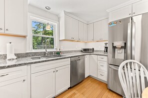 A modern kitchen with white cabinets, a stainless steel refrigerator, a dishwasher, and a granite countertop.