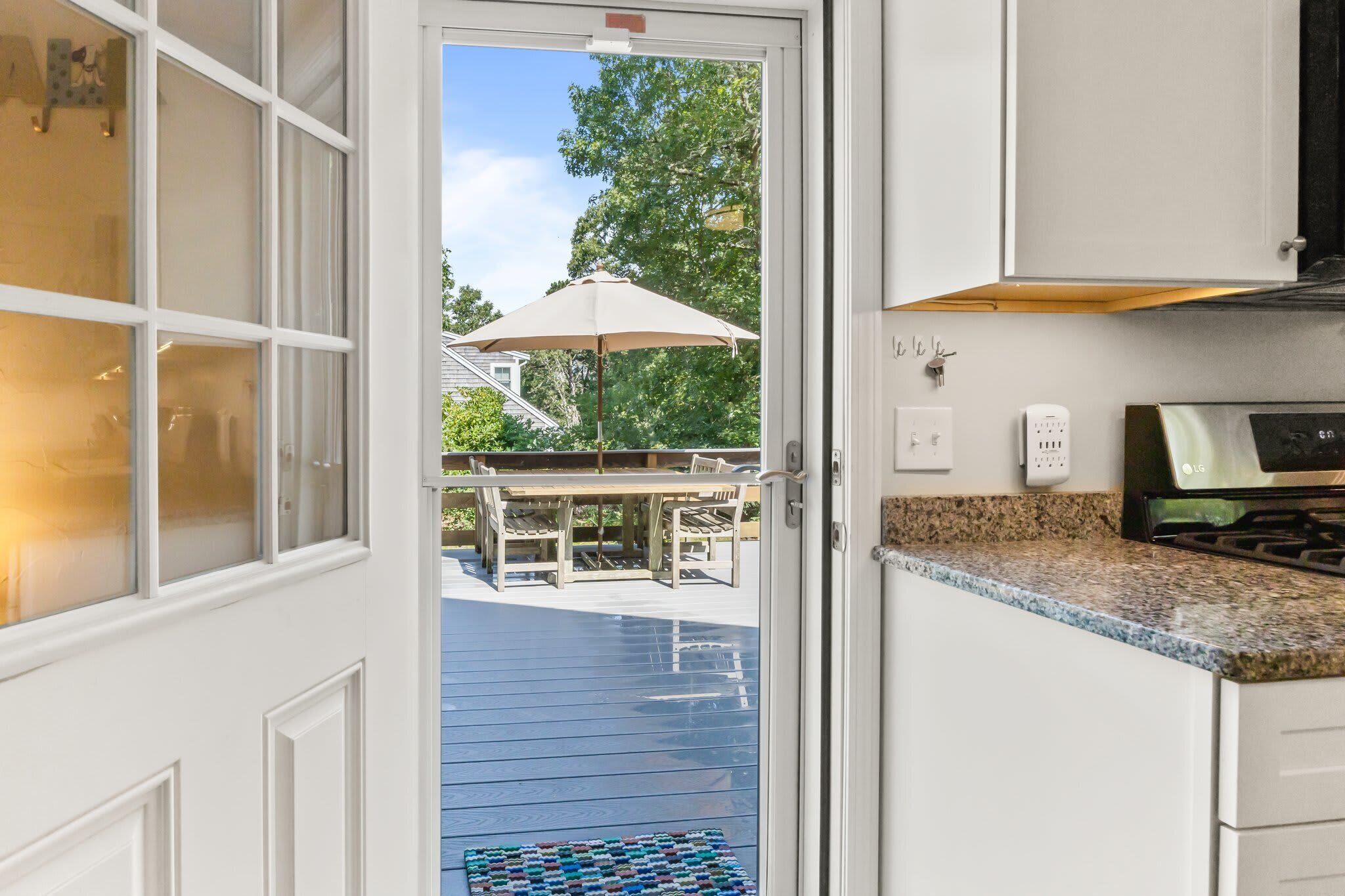 A kitchen with white cabinetry, a granite countertop, an outdoor patio with a table and chairs, and a view of a house with a tree.
