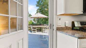 A kitchen with white cabinetry, a granite countertop, an outdoor patio with a table and chairs, and a view of a house with a tree.
