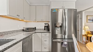 Una cucina moderna con elettrodomestici in acciaio inossidabile, mobili bianchi, lavastoviglie integrata e un piano di lavoro in granito.