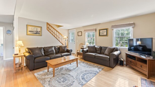 A spacious living room with two leather sofas, a wooden coffee table, a television, and a staircase. - Cape Cod Cottage Near Beaches & Bike Trail (Harwich)