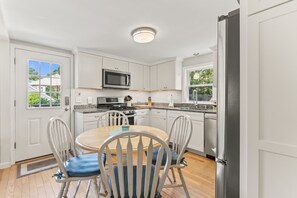 Een moderne keuken met witte kastjes, een magnetron, fornuis en een eethoek met een ronde tafel en stoelen.