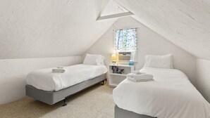 A bedroom with two beds, a window with curtains, a bedside table with books, and a radiator. - Cape Cod Cottage Near Beaches & Bike Trail (Harwich)