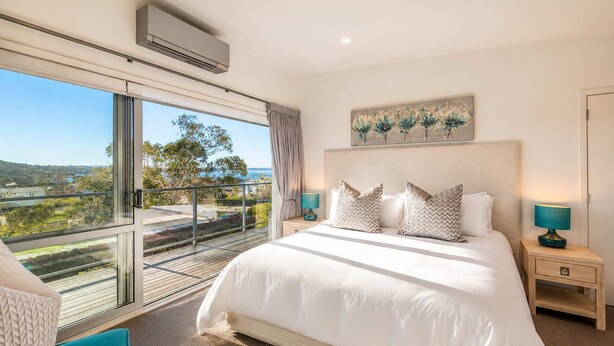 A bedroom with a large bed, two bedside tables, a ceiling fan, and a view of the outdoors.