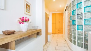A hallway with a wooden bench, a white vase with flowers, a framed picture, and a door leading to a room with a tiled floor. - Twin House - Le Lecce (Capoliveri)
