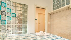 A bedroom with a bed, a bathroom door, and a wall with glass blocks. - Twin House - Le Lecce (Capoliveri)