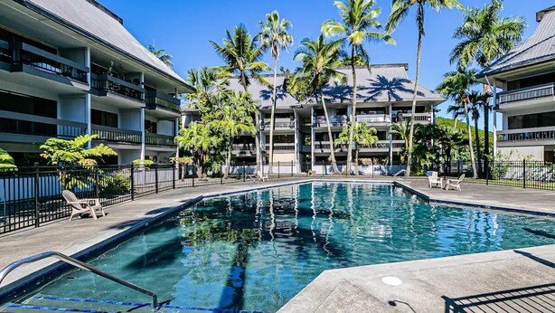 A hotel pool area with a clear blue pool, surrounded by palm trees and a multi-story building with balconies. - Waiakea Villas Gem. Shared Pool & Private Balcony!
 (Hilo)