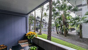 A balcony with a table set for dining, featuring a vase with sunflowers and a bowl of green apples. - Waiakea Villas Gem. Shared Pool & Private Balcony!
 (Hilo)