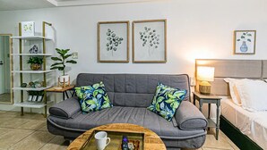 A modern living room with a grey sofa, two decorative wall art pieces, a wooden coffee table, and a bedside table with a lamp. - Waiakea Villas Gem. Shared Pool & Private Balcony!
 (Hilo)