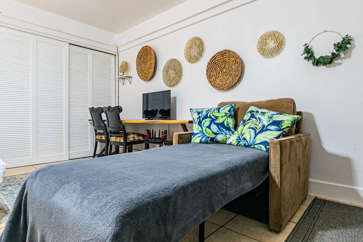 Quarto com cama, escrivaninha e cadeira. Há painéis decorativos na parede e uma planta.