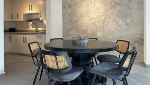 Un comedor moderno con una mesa redonda y seis sillas, una cocina al fondo y una pared con textura.