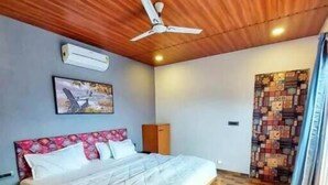 A bedroom with a wooden ceiling, a bed, a ceiling fan, and a wall with a patterned tapestry. - Wandr Tryo Villa Karjat (Khalapur)
