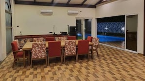 A dining area with a checkered floor, wooden tables, and red upholstered chairs. - Wandr Tryo Villa Karjat (Khalapur)