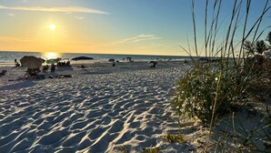 Una playa con sombrillas y gente, un cielo despejado y el sol poniéndose o saliendo.