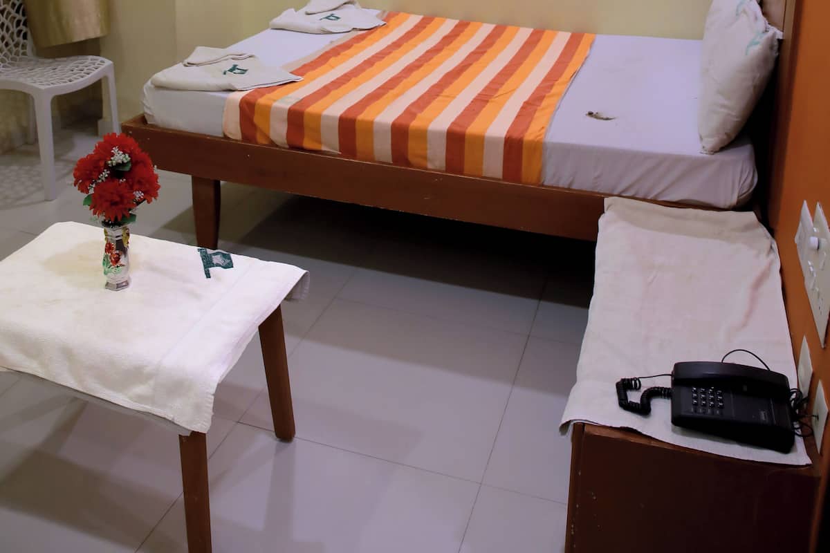 A hotel room with a bed, a small table with a vase, a telephone on a table, and an air conditioning unit on the wall.