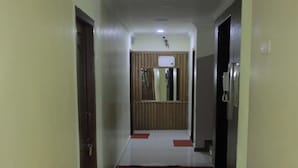 Un couloir doté d’un sol carrelé, une porte en bois sur la gauche, un miroir avec un cadre en bois et une moquette rouge menant à une pièce.